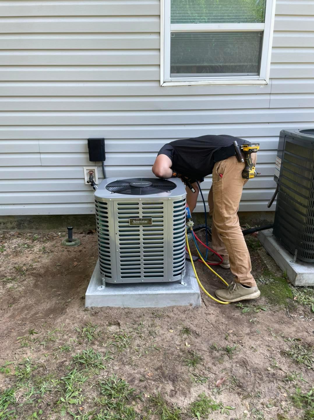 A person servicing an outdoor residential air conditioning unit with gauges and hoses attached