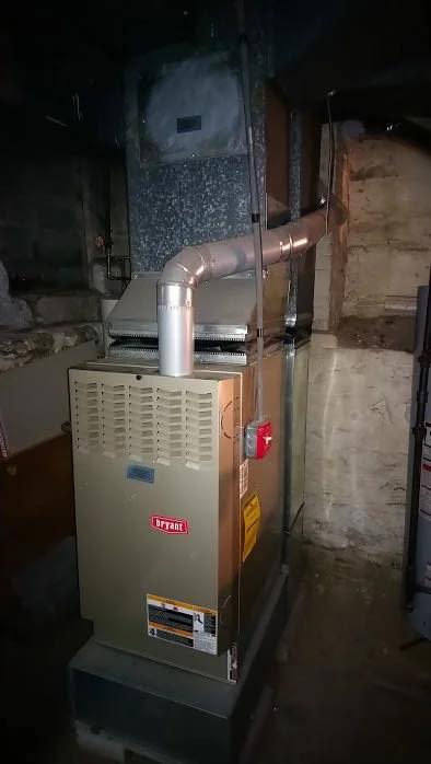 Bryant gas furnace with ductwork on a concrete platform in a dim basement utility room
