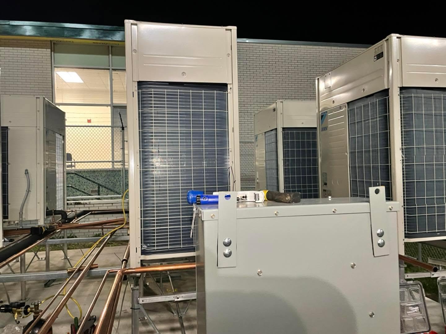 Commercial rooftop HVAC condenser units with copper refrigerant piping and service tools at night