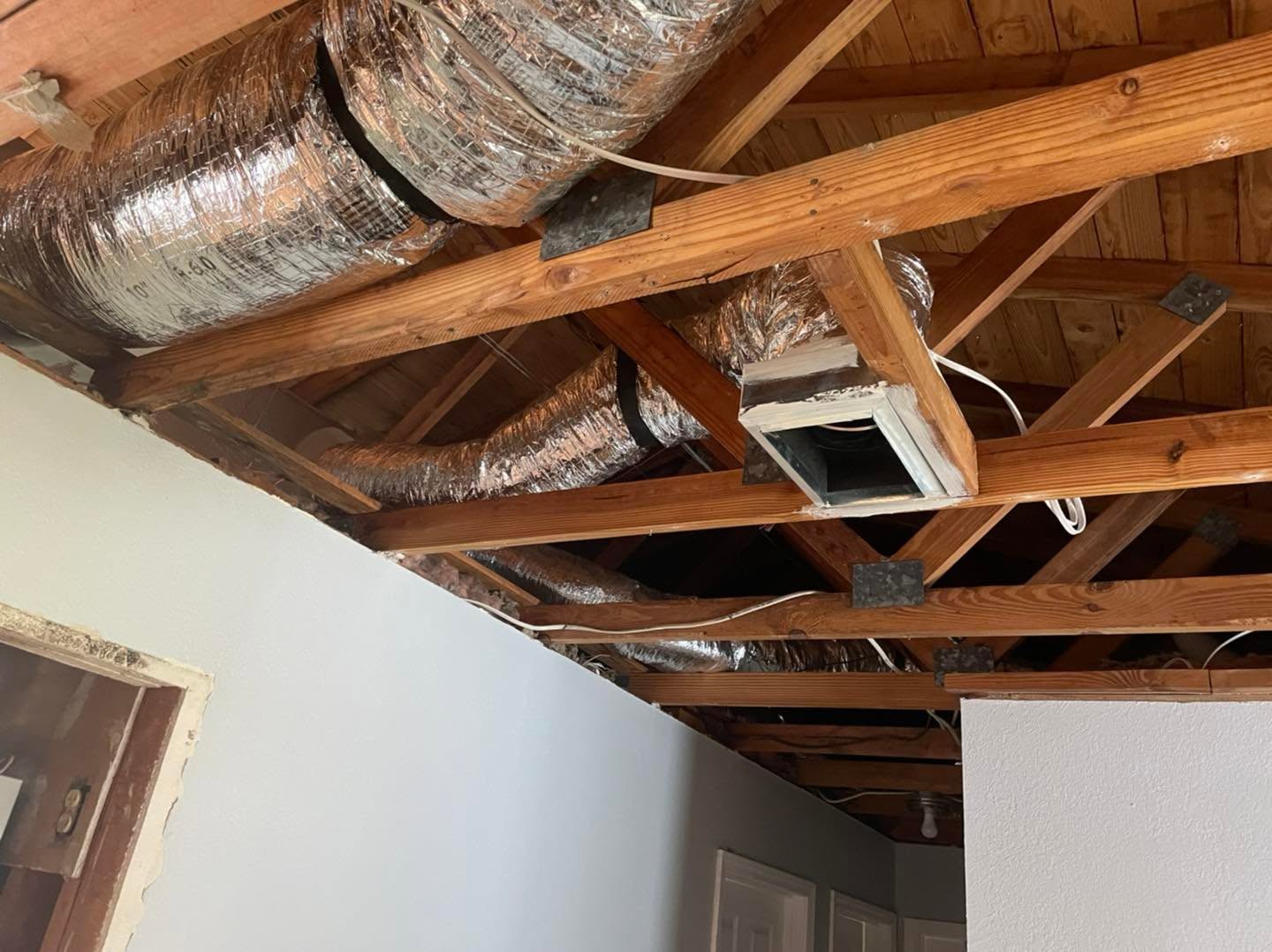 Exposed ceiling with wooden joists, flexible foil HVAC ducts and rectangular vent box during home renovation