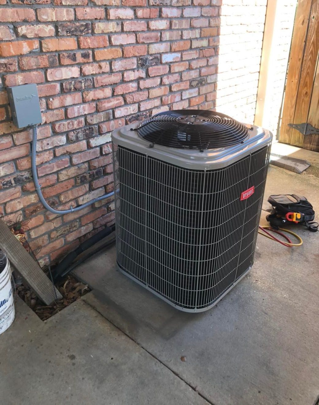 Bryant outdoor air conditioning unit on concrete pad beside brick wall with service tools nearby