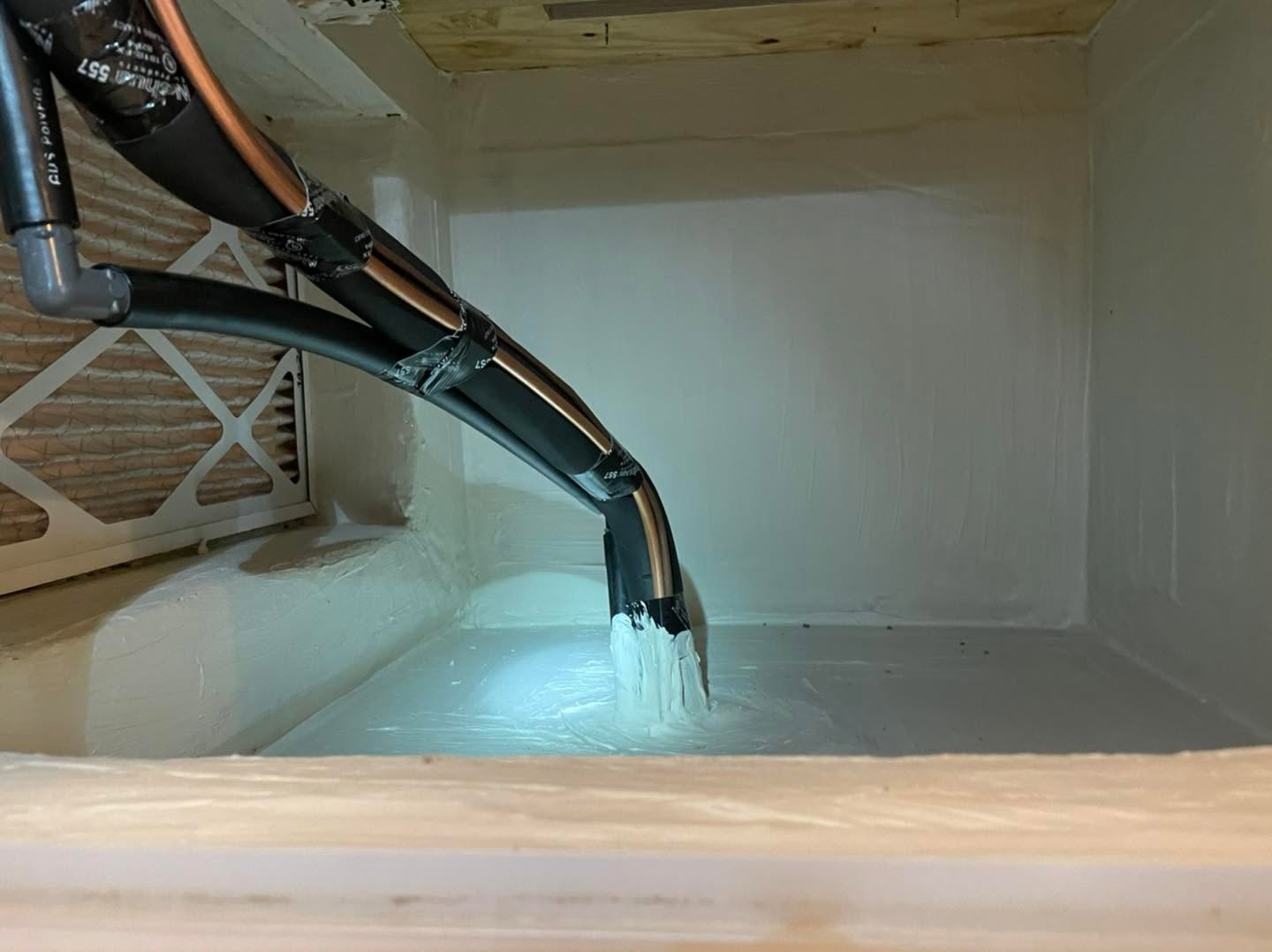 Insulated copper HVAC refrigerant lines sealed with white foam entering a painted equipment cavity beside an air filter