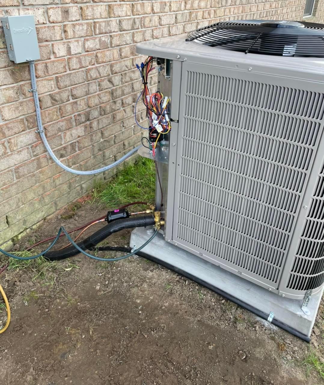 Outdoor HVAC condensing unit with exposed wiring and refrigerant lines by brick house pad