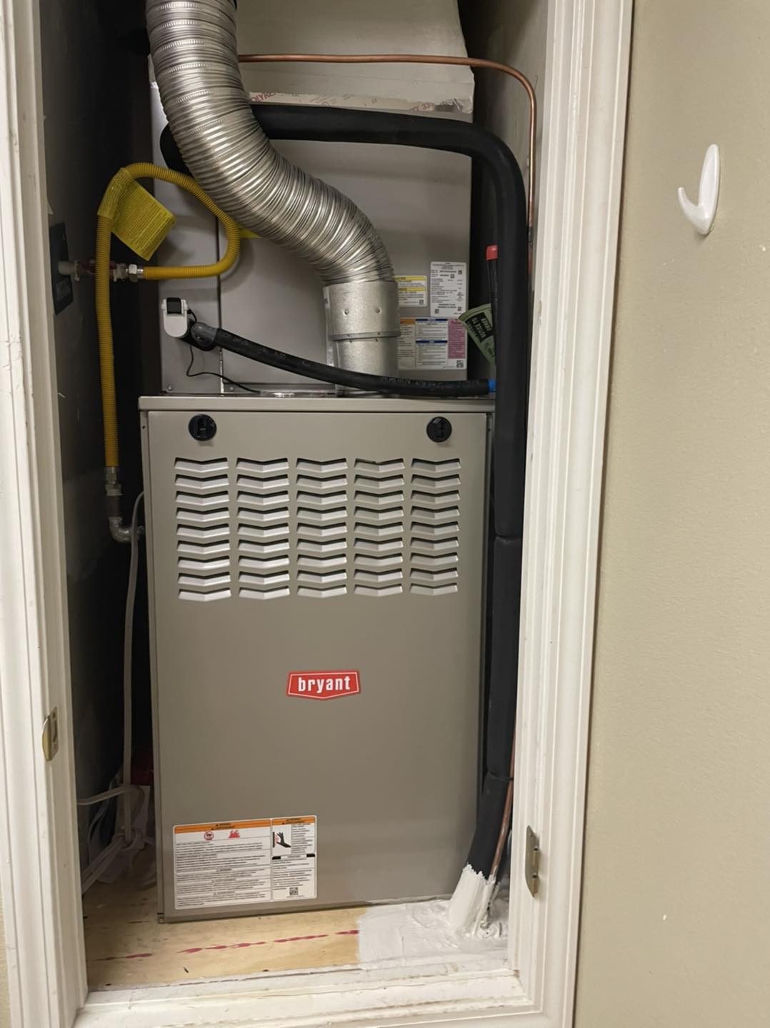 Bryant furnace in utility closet with silver exhaust duct, yellow gas line, and black insulated refrigerant lines.