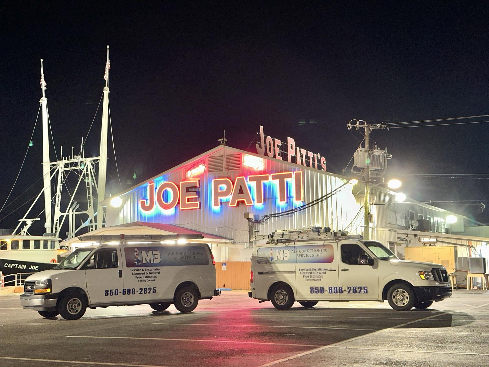 Joe Patti's neon-lit building at night with two service vans parked in front and boat masts in background