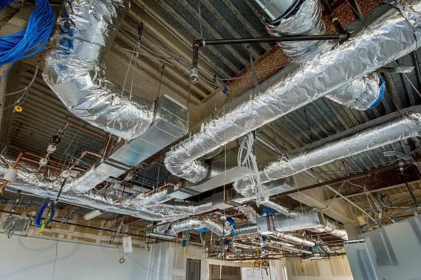 Silver foil-wrapped HVAC ducts and piping on exposed ceiling in commercial building under construction
