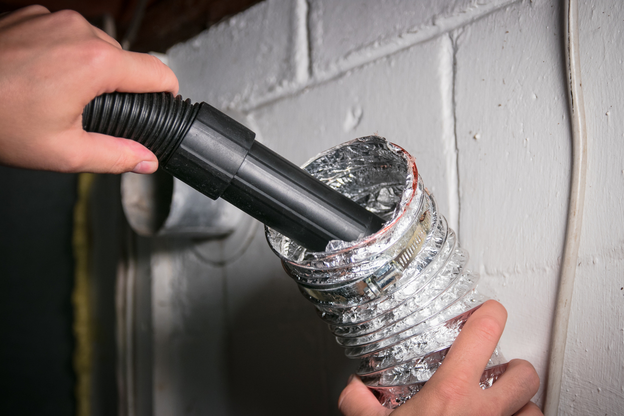 A person vacuuming a flexible dryer vent duct to remove lint buildup