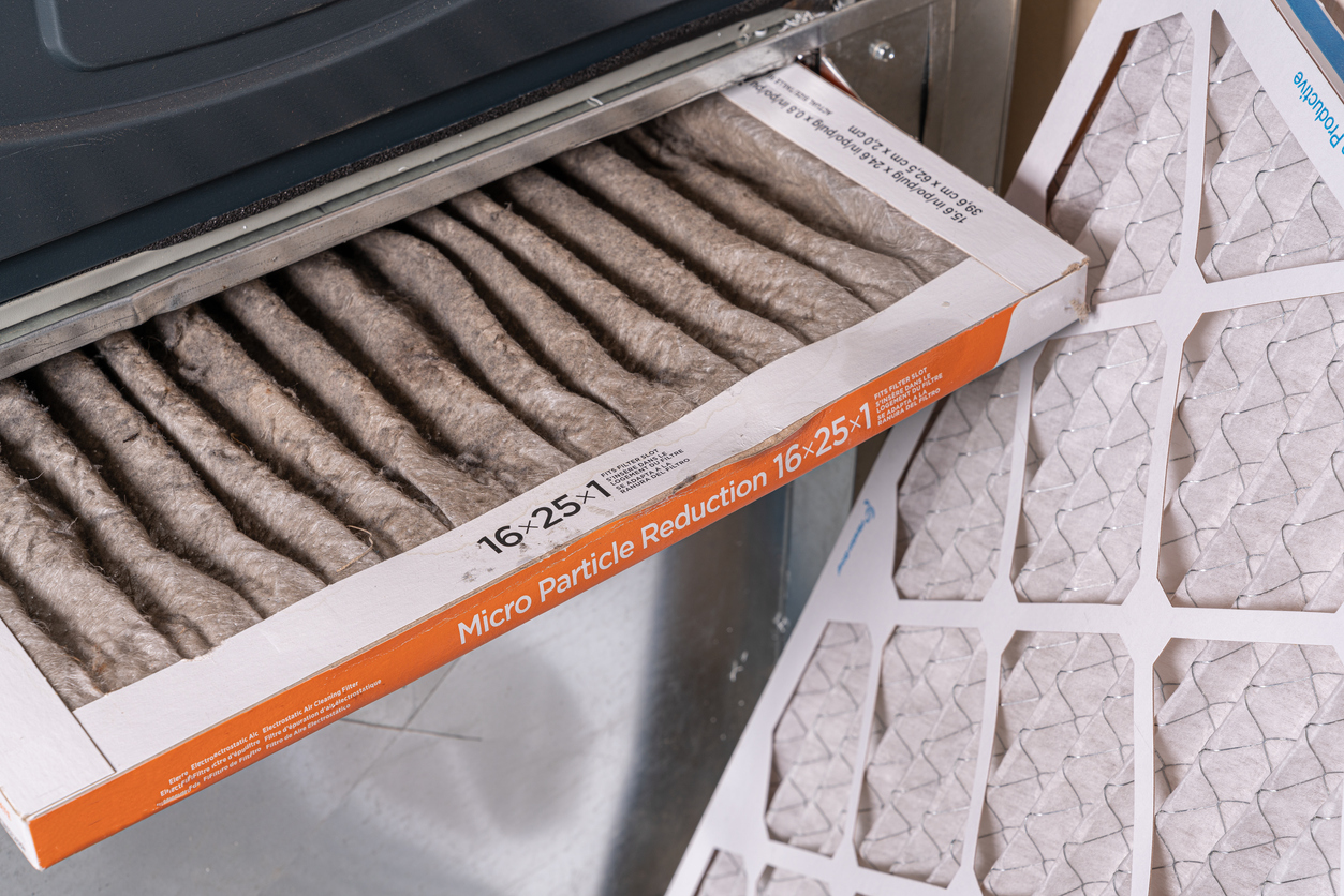Dirty 16x25x1 HVAC air filter partially removed showing dust buildup beside a new pleated air filter