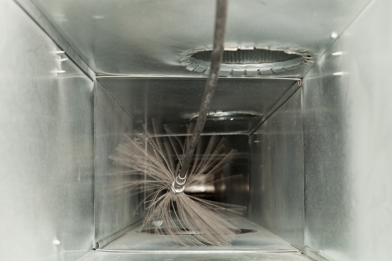 Rotating brush on rod cleaning the inside of a rectangular metal HVAC duct