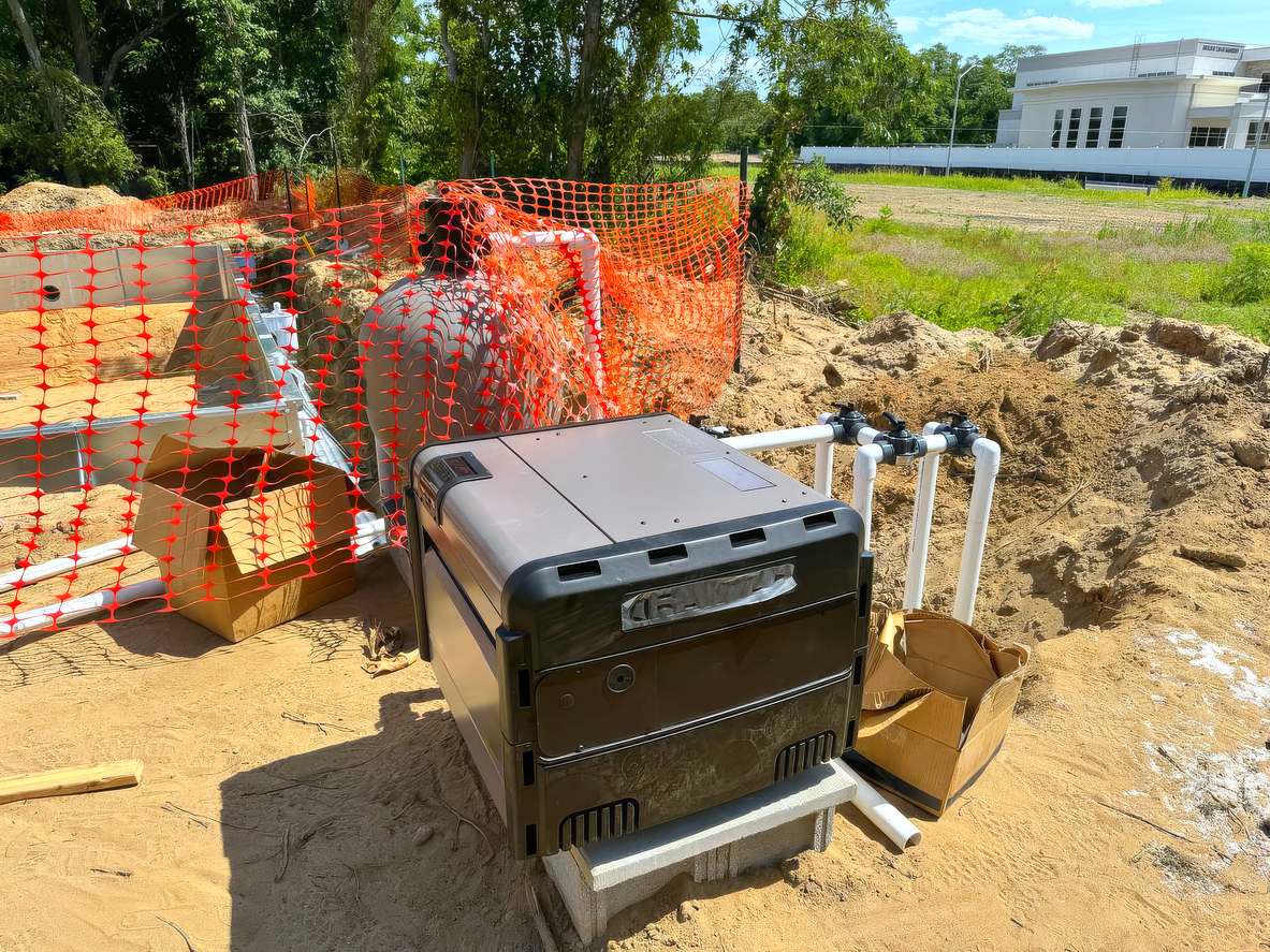 Pool equipment and PVC piping on cinder blocks at a sandy construction site with orange safety fencing