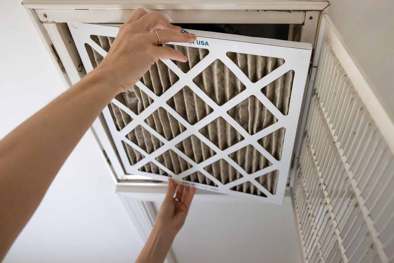 A person replacing a dirty HVAC air filter in a ceiling return vent