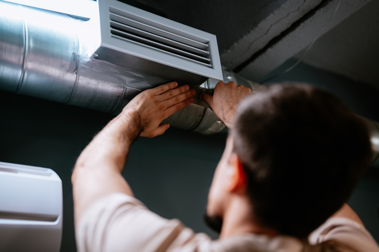 A man installing HVAC ductwork and ceiling vent, securing metal duct with tape