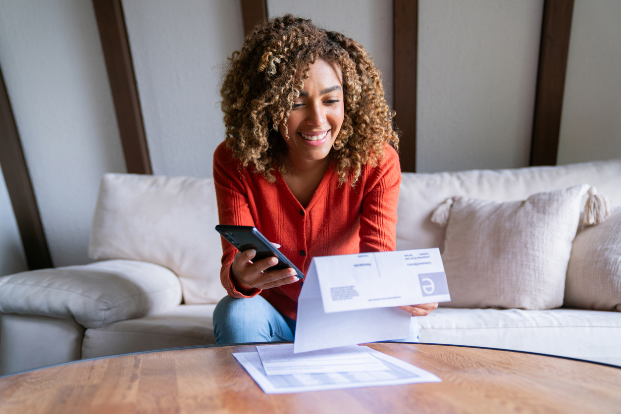 Smiling woman on couch scanning a bill with her smartphone to manage monthly finances