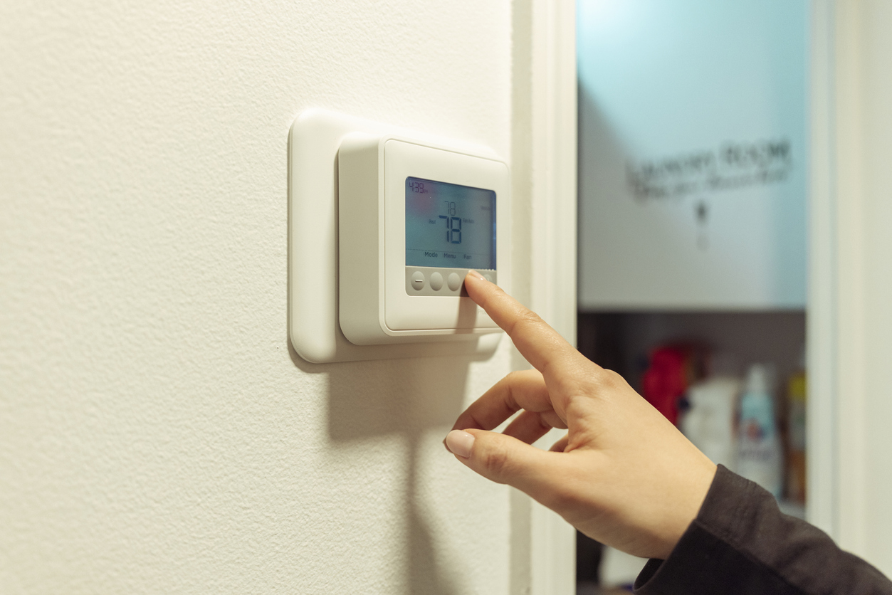 a person adjusting digital thermostat set to 78°F on white wall