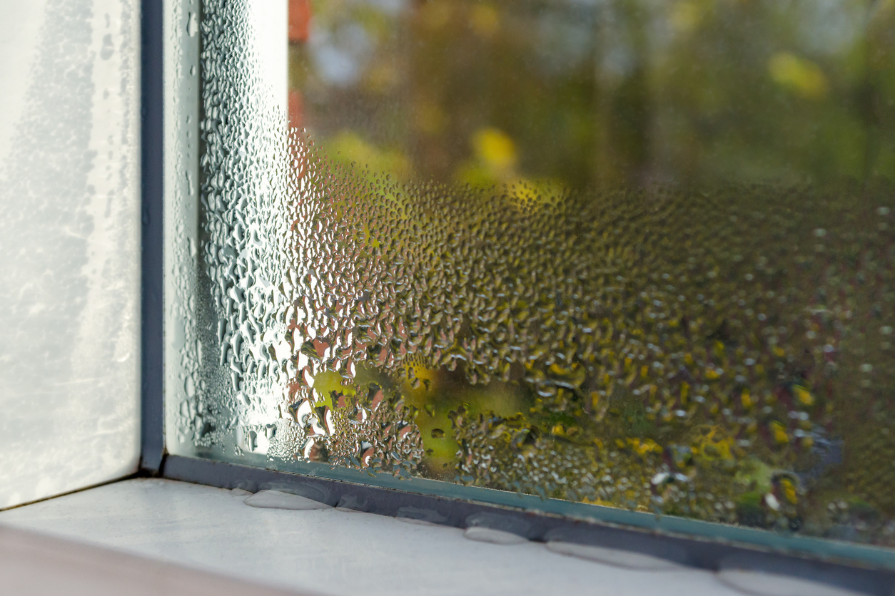 Window sill with condensation and water droplets on glass, blurred autumn foliage visible outside